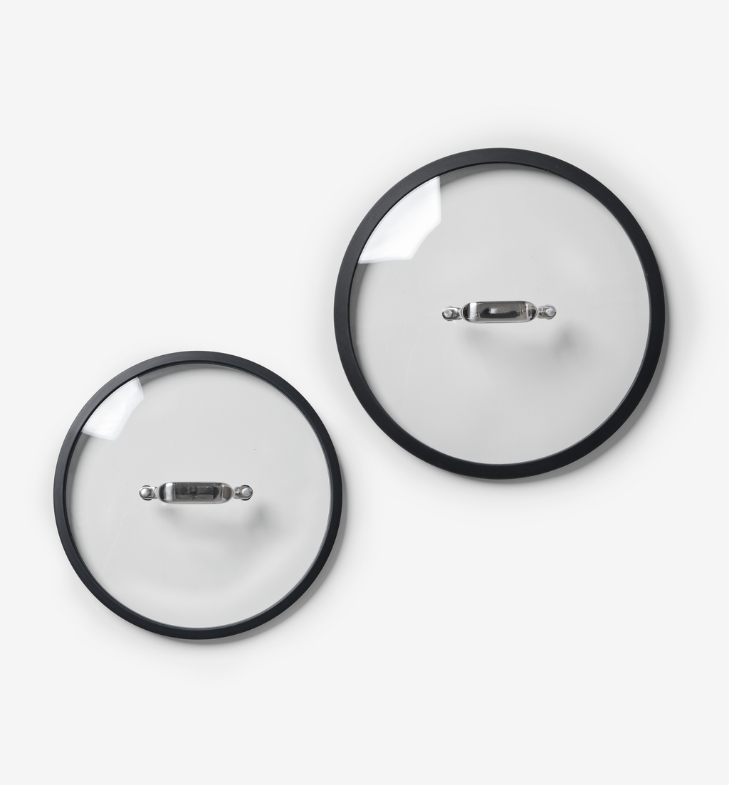 Two glass pot lids with black rim and stainless steel handles, top-down view